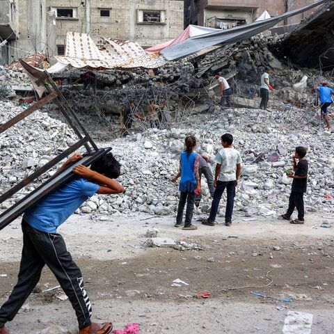 A boy walks carrying a table on his back past salvage workers scrapping the rubble of a building that was destroyed during Israel's war against Hamas in Gaza City on Aug. 16, 2026. — Photo by Omar Al-Qattaa / AFP via Getty Images