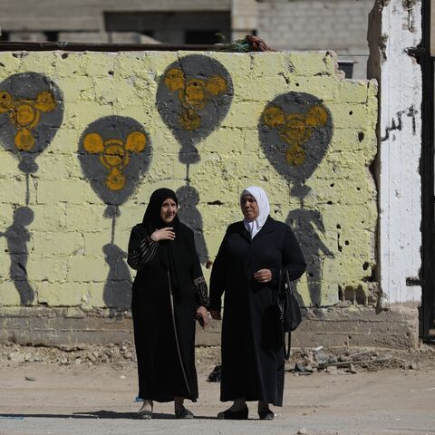 Two women stand before graffiti on the cemetery wall for victims of the chemical massacre, on Aug. 21, 2025 in Zamalka, Syria. 
