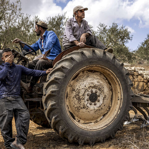 Palestinian men sitting in and by a tractor look on after another man was injured by gunfire whilst being chased away by Israeli forces, in Aqraba in the Israeli-occupied West Bank on Oct. 6, 2026.