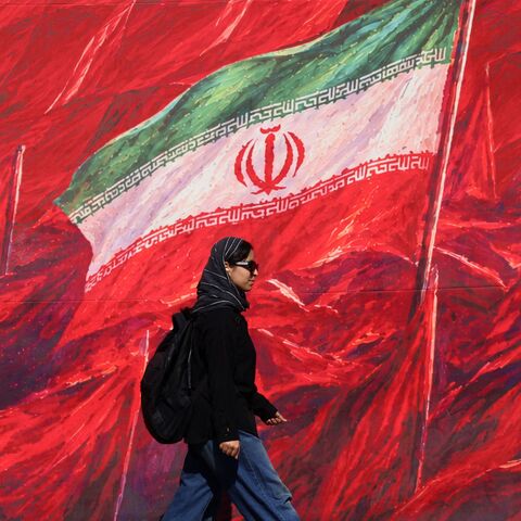 A woman walks past a mural bearing the Iranian national flag