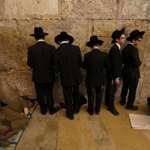 An Israeli soldier sleeps as ultra-Orthodox Jewish youths pray on Tisha B'Av at the Western Wall, Judaism's holiest prayer site, in Jerusalem's Old City July 16, 2013. Tisha B'Av, a day of fasting and lament, is traditionally the date in the Jewish calendar on which the First and Second Temples were destroyed, respectively in the sixth century B.C. by the Babylonians and the first century A.D. by the Romans. REUTERS/Baz Ratner (JERUSALEM - Tags: RELIGION TPX IMAGES OF THE DAY) - RTX11O0M