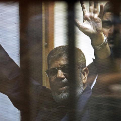 Deposed Egyptian President Mohamed Mursi greets his lawyers and people from behind bars after his verdict at a court on the outskirts of Cairo, Egypt June 16, 2015. An Egyptian court sentenced deposed President Mohamed Mursi to death on Tuesday on charges of killing, kidnapping and other offences during a 2011 mass jail break.The general guide of the Muslim Brotherhood, Mohamed Badie, and four other Brotherhood leaders were also handed the death penalty. More than 80 others were sentenced to death in absent