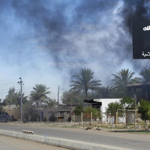 Smoke raises behind an Islamic State flag after Iraqi security forces and Shiite fighters took control of Saadiya in Diyala province from Islamist State militants, November 24, 2014. Iraqi forces said on Sunday they retook two towns north of Baghdad from Islamic State fighters, driving them from strongholds they had held for months and clearing a main road from the capital to Iran. There was no independent confirmation that the army, Shi'ite militia and Kurdish peshmerga forces had completely retaken Jalawl