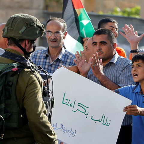 A Palestinian boy holds a sign that reads "we demand our dignity" in front of  Israeli soldiers during a protest calling for the reopening of a closed street in the West Bank city of Hebron August 24, 2016.  REUTERS/Mussa Qawasma  - RTX2MW1E