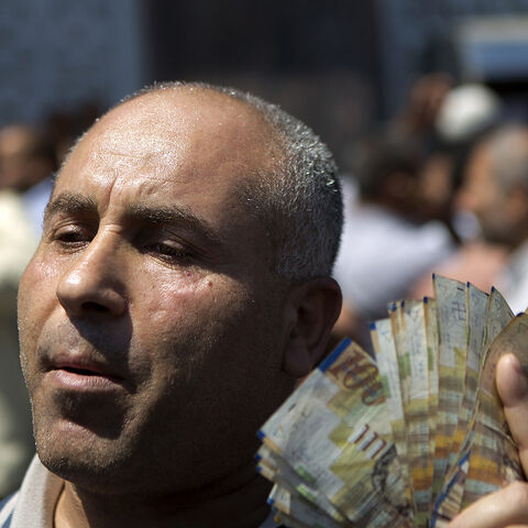 A civil servant paid by the Palestinian Authority displays New Israeli Shekels (NIS) bills after he took his salary from a bank in Gaza City on June 11, 2014. Gaza's banks reopened today after being closed for six days by Hamas forces in a row over pay which was the first hitch in a reconciliation deal between Hamas and the Palestine Liberation Organisation that began with the formation of a new unity government. The PA has so far refused to pay Hamas's 50,000 civil servants, who are not registered as its e