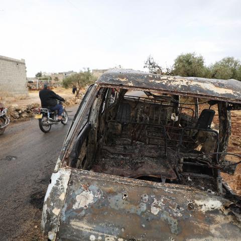A picture taken on October 28, 2019 shows Syrian bikers riding past a damaged car at the site of a suspected US-led operation against Islamic State (IS) chief Abu Bakr al-Baghdadi the previous day, on the edge of the small Syrian village of Barisha in the country's opposition-held northwestern Idlib province. - US President Donald Trump announced that Baghdadi, the elusive leader of the jihadist group and the world's most wanted man, was killed in the early hours of Octobe 27 in an overnight US raid near th