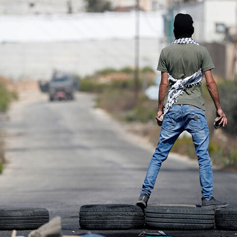 A demonstrator stands on tires in front of Israeli forces during a protest to show solidarity with Palestinian prisoners held in Israeli jails, near the Jewish settlement of Beit El in the Israeli-occupied West Bank October 1, 2019. REUTERS/Mohamad Torokman - RC1E64FD2C50