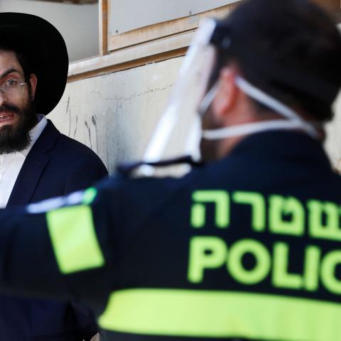 An Israeli police officer speaks to an ultra-Orthodox Jewish student at a Yeshiva (Talmudic school) in Bnei Barak, a city east of Tel Aviv with a significant ultra-Orthodox Jewish population, on April 2, 2020, as part of measures imposed by Israeli authorities against the COVID-19 coronavirus pandemic. - Israeli police backed by surveillance helicopters have stepped up patrols of ultra-Orthodox Jewish neighbourhoods that have become coronavirus hotspots. (Photo by JACK GUEZ / AFP) (Photo by JACK GUEZ/AFP vi