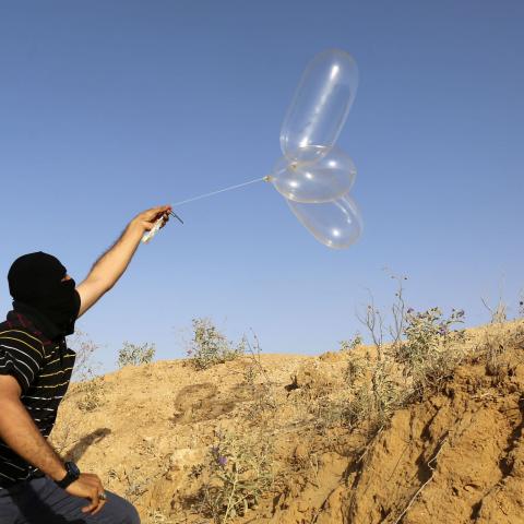 A masked Palestinian launches a Balloon loaded with flammable materials to be flown toward Israel, at the Israel-Gaza border, in Rafah in the southern Gaza Strip on June 17, 2018. (Photo by SAID KHATIB / AFP)        (Photo credit should read SAID KHATIB/AFP via Getty Images)