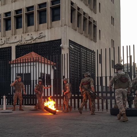 Lebanese Army soldiers roll away a flaming tire from the fence surrounding the local branch of the Banque du Liban (Lebanese Central Bank) as protesters gather to demonstrate against dire economic conditions in the northern city of Tripoli on June 11, 2020. - The Lebanese pound sank to a record low on the black market on June 11 despite the authorities' attempts to halt the plunge of the crisis-hit country's currency, money changers said. Lebanon is in the grips of its worst economic turmoil in decades, and