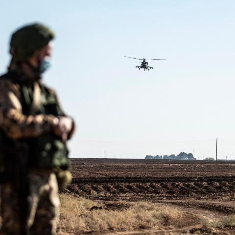 A Russian Mil Mi-17 military helicopter flies by a soldier during a joint Russian-Turkish patrol convoy in the eastern countryside of the town of Darbasiyah near the border with Turkey in Syria's northeastern Hasakah province on December 7, 2020. (Photo by Delil SOULEIMAN / AFP) (Photo by DELIL SOULEIMAN/AFP via Getty Images)