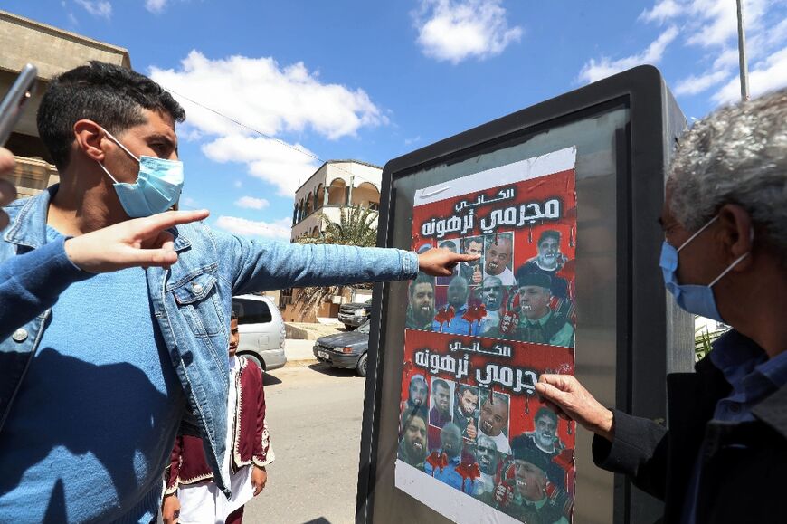 Libyans point at a poster depicting members of the al-Kani family who commanded a militia that terrorised the people of Tarhuna, during a funeral procession for 12 victims, on March 26, 2021