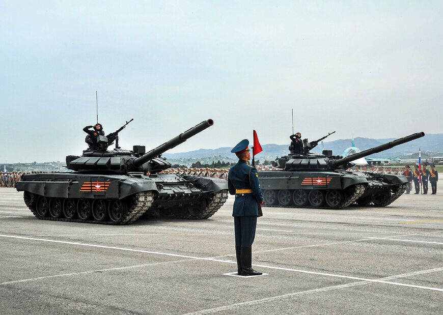 A handout picture from the Syrian Arab News shows a Russian soldier standing by T-90 battle tanks during the Victory Day military parade, in May 2021, at the Russian military Hmeimim base, southeast of the Syrian port of Latakia