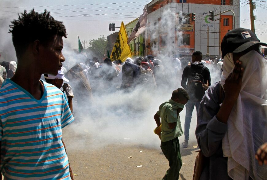 Sudanese protesters take cover from tear gas fired by security forces during demonstrations against the military administration, in Khartoum on March 14, 2022