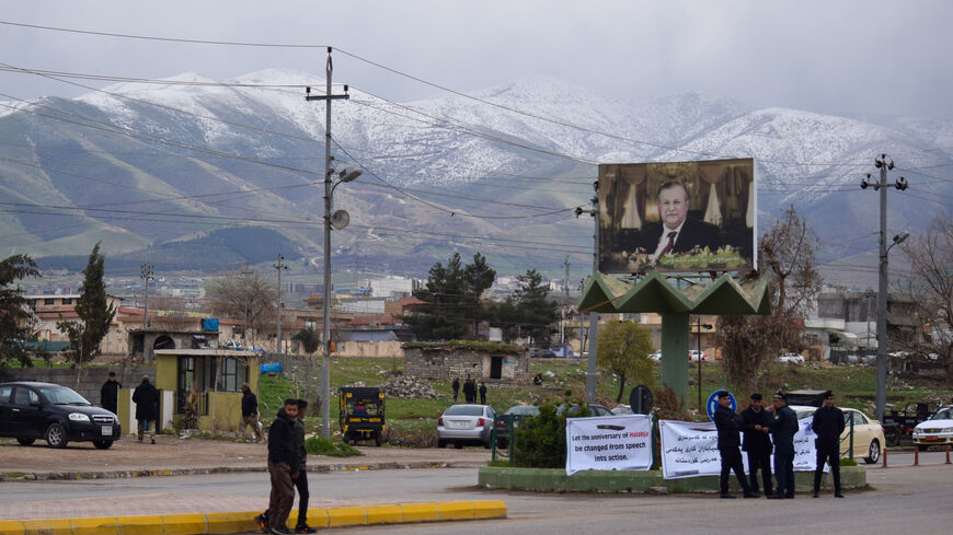 A sign reading "Let the Anniversary of Halabja be changed from speech into action" hangs beneath a poster of late Patriotic Union of Kurdistan leader Jalal Talabani in Halabja on March 16, 2022. Winthrop Rodgers/Metrography