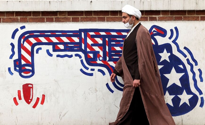 An Iranian cleric walks past an anti-American mural on a wall of the former US embassy in Tehran, as the rival nations seek to revive a nuclear accord