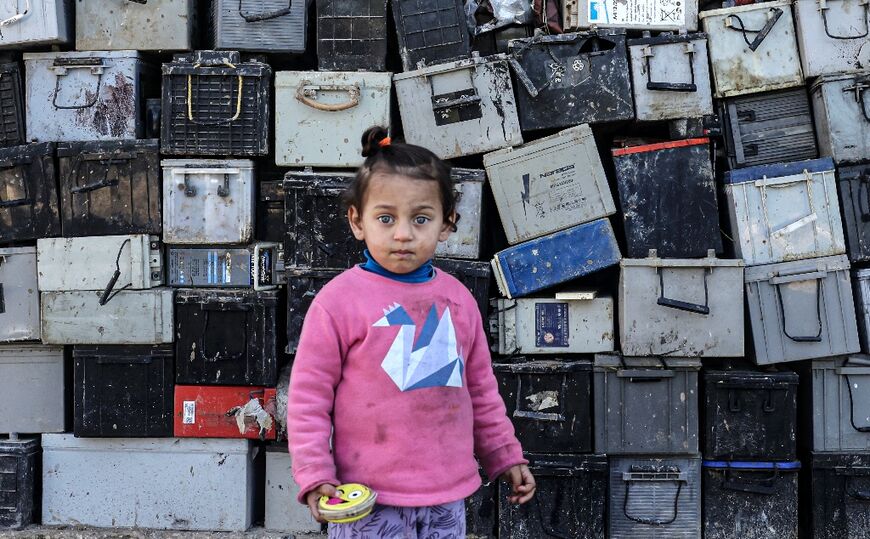 A Palestinian girl stands next to a stack of discarded batteries; Israel used to play a role in managing toxic materials from Gaza, but that stopped with the Hamas takeover in 2007