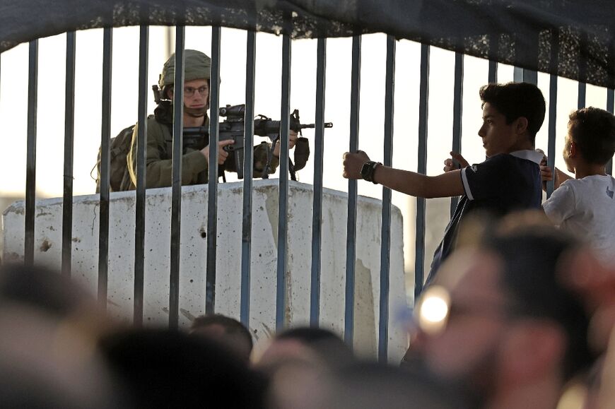 An Israeli soldier stands guard as Palestinians arrive at the Qalandia checkpoint in the occupied West Bank to reach Jerusalem's Al-Aqsa Mosque on April 27