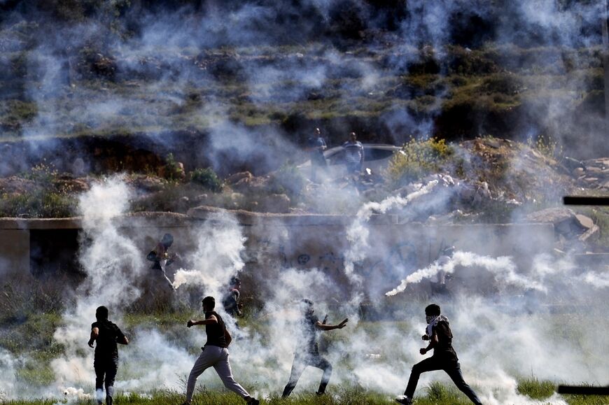 Palestinians run for cover from tear gas during clashes with Israeli security forces at the northern entrance to the West Bank city of Ramallah