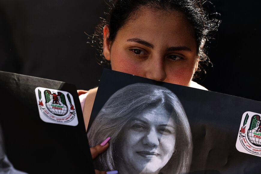 A Palestinian woman holds a photograph of slain veteran Al Jazeera journalist Shireen Abu Akleh, as her body is carried toward the offices of the news channel in the West Bank city of Ramallah, on May 11, 2022