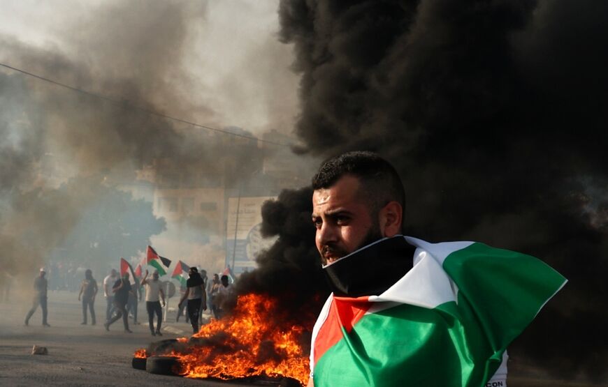 A protester draped in a Palestinian flag looks on during clashes with Israeli forces near Nablus in the occupied West Bank