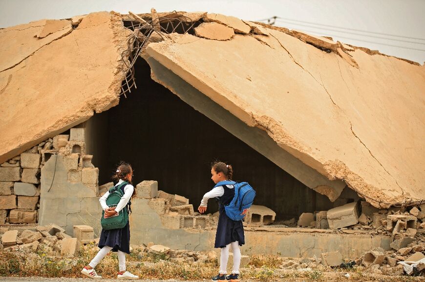 Iraqi pupils walk past a destroyed house in Habash