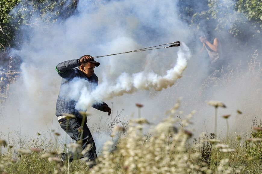A Palestinian protester uses a slingshot to hurl back a tear gas canister at Israeli security forces following a march marking 74 years since the "Nakba" or "catastrophe" of Israels' creation, near Ramallah in the occupied West, Bank May 15, 2022