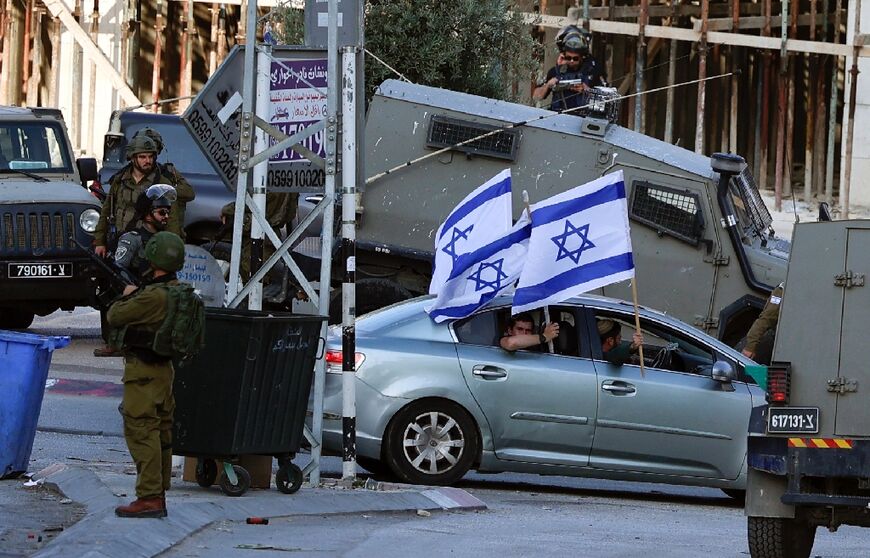 Israeli security forces look on as Jewish settlers enter the occupied West Bank town of Huwara waving Israeli flags from their car, on May 25, 2022