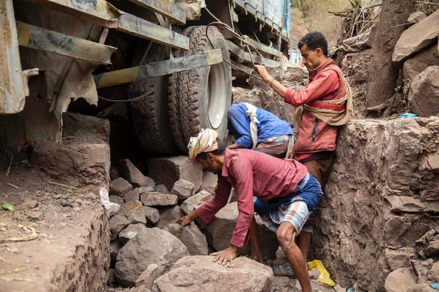 Yemeni men try to move a vehicle stuck on a heavily damaged narrow road that serves as a lifeline for Yemen's third-largest city of Taez