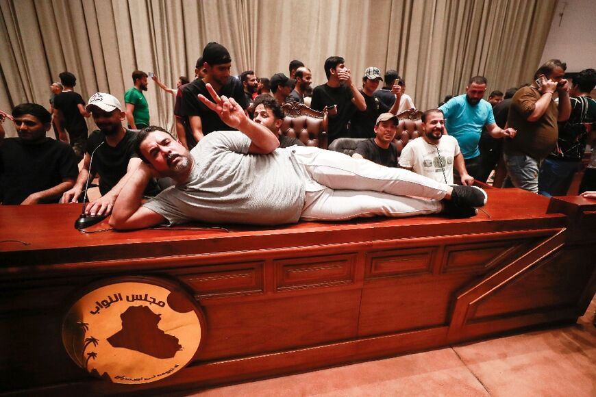 A protester lying on the Iraqi parliament speaker's desk flashes a V-for-victory sign with his fingers