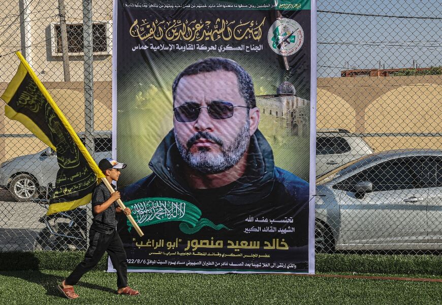 A Palestinian boy holding an Islamic Jihad flag walks during a mourning gathering in Rafah past a picture of Khaled Mansour, a senior leader of the group, who was killed in the Israel-Gaza fighting