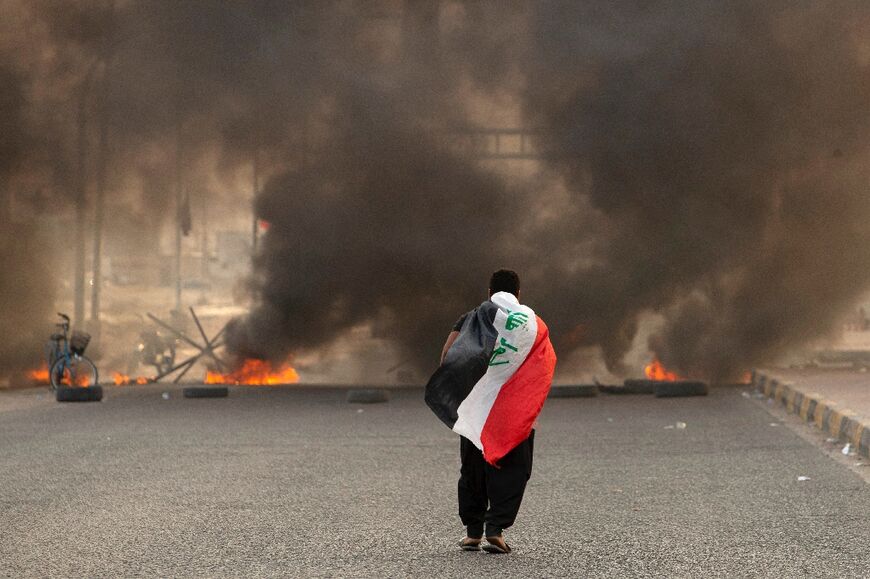 A supporter of Iraqi Shiite cleric Moqtada Sadr carries the Iraqi flag as he walks down a road blocked by burning tyres during a demonstration in Iraq's southern city of Basra