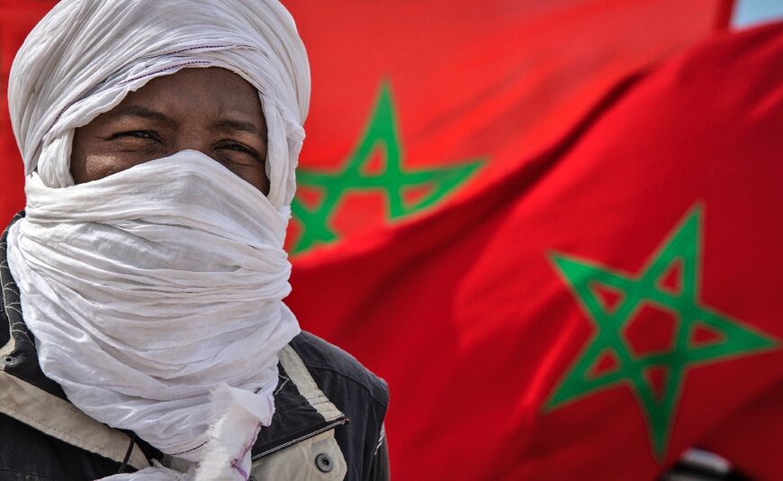 A tribesman stand in front of a Moroccan flag near the border in Guerguerat located in the Western Sahara, on November 26, 2020, after an intervention of the royal Moroccan armed forces in the area