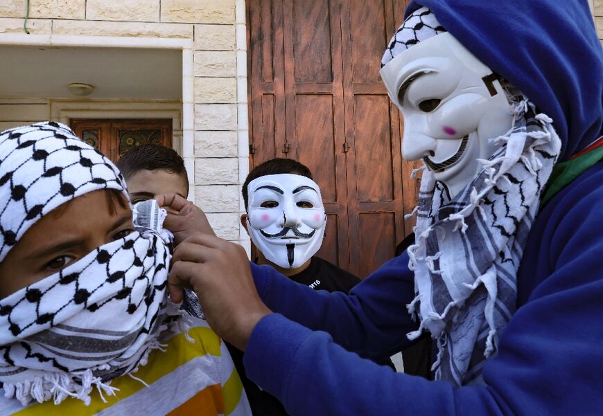 A Palestinian youth wearing a mask helps another to fit his headdress in Al-Aroub refugee camp, north of the occupied West Bank city of Hebron on Thursday