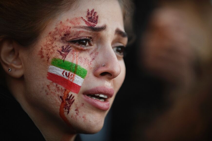 A demonstrator with an Iranian flag and red hands painted on her face at a rally in support of Iranian protests, in Paris on October 9, 2022