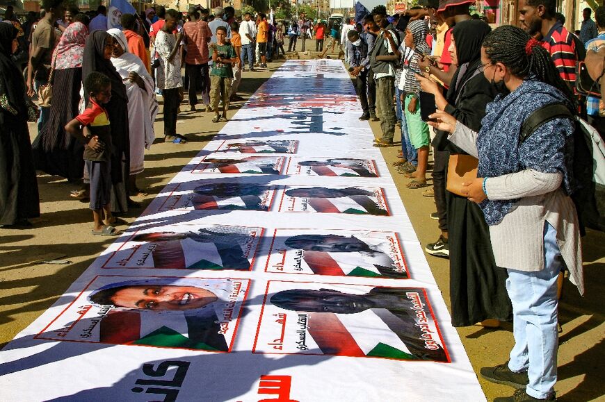 Sudanese protesters lay out a banner bearing pictures of those killed since last year's military coup