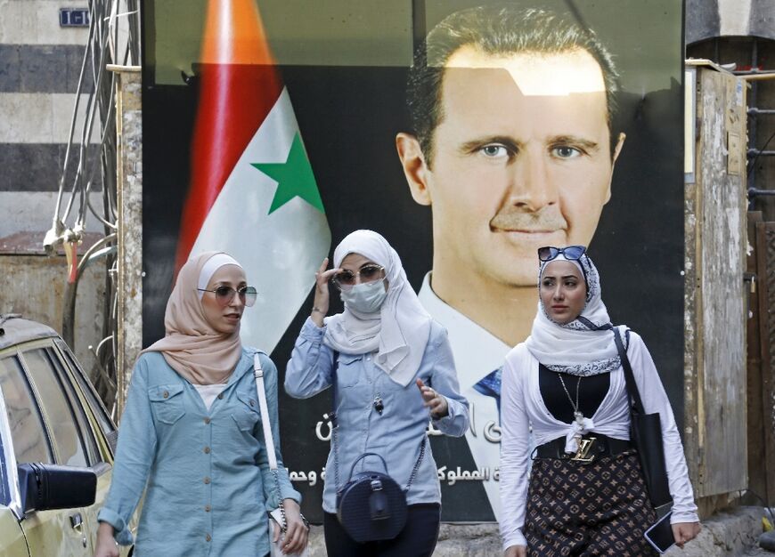 Syrians walk in front of a poster of President Bashar al-Assad near the Grand Umayyad Mosque in Damascus on September 23, 2021