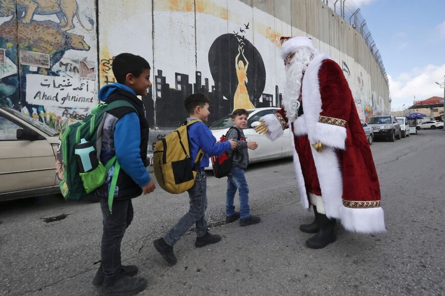 A man dressed as Santa Claus greets children on a street alongside Israel's separation wall in the occupied West Bank city of Bethlehem