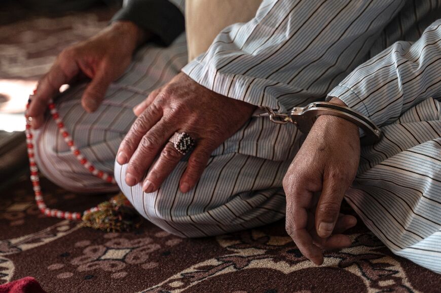 An Afghan man, sentenced to death for murder, grasps a string of prayer beads in his handcuffed hands