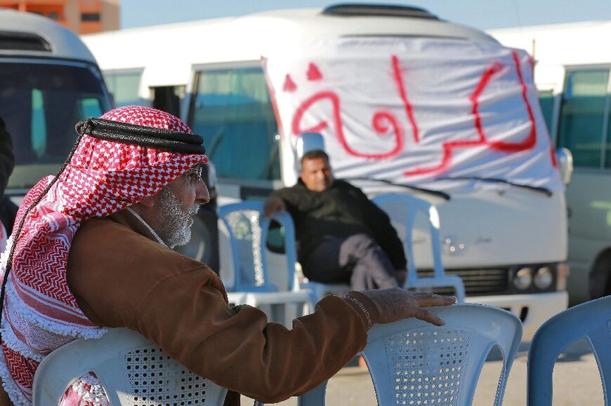 Striking Jordanian bus drivers sit next to a banner reading "dignity" in Arabic 
