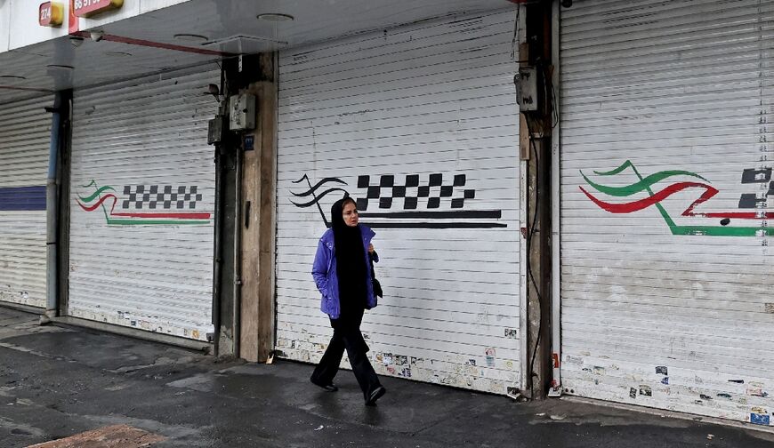 A woman walks past a closed shop along Satarkhan Street in Iran's capital Tehran, after calls on social media for a three-day strike