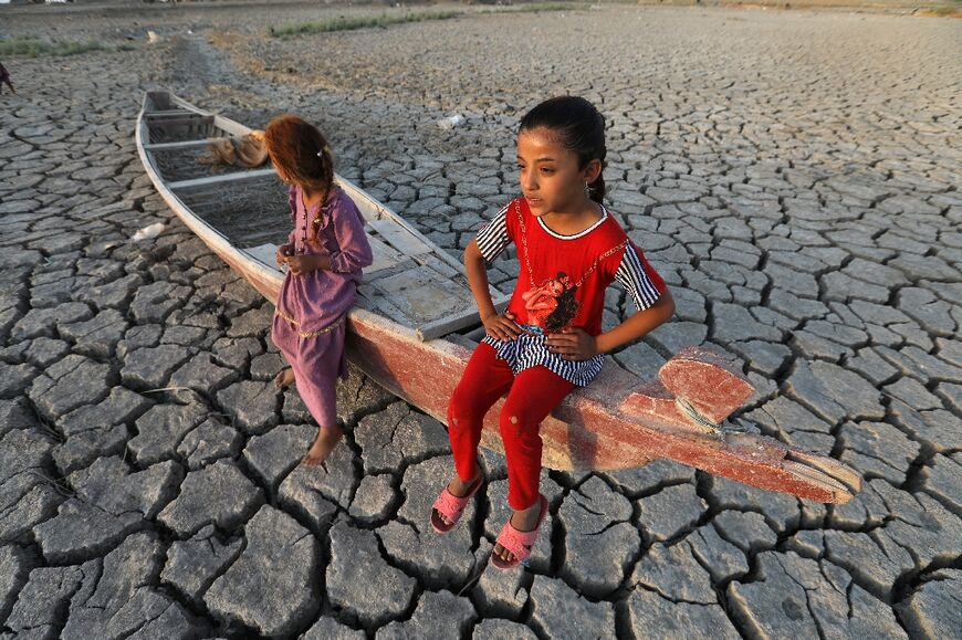 Children sit atop a boat lying on dried and cracked soil in a section of the Chibayish marshes in July 2022