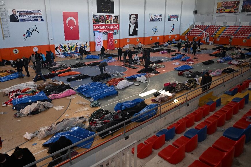 People walk past the bodies of victims stored at a sports hall in the southeastern Turkish city of Kahramanmaras