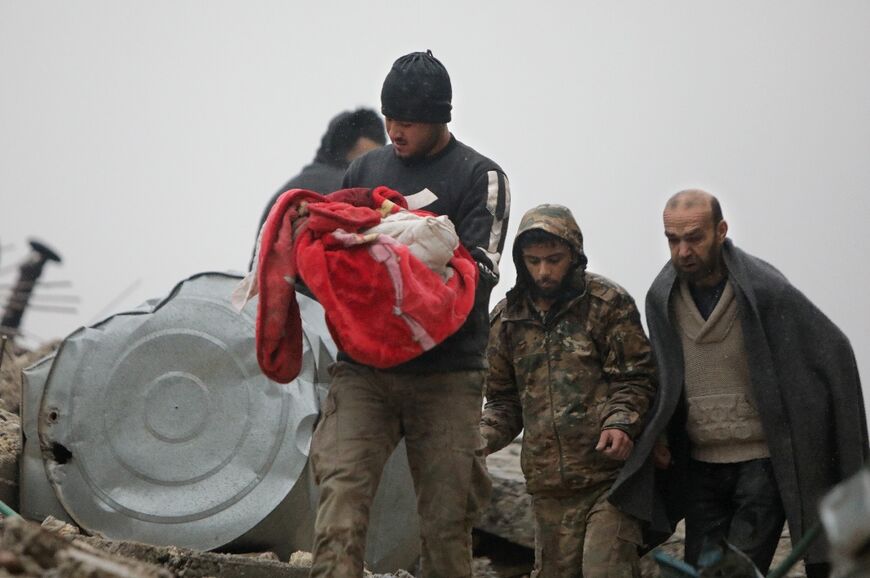 A Syrian man carries the body of an infant who was killed in an earthquake in the town of Jandairis