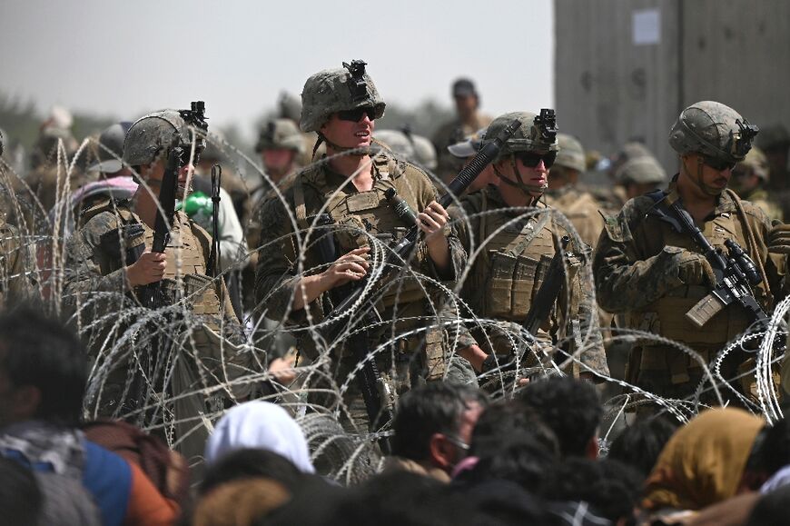 US soldiers stand guard behind barbed wire as Afghans sit on a roadside near the military part of the airport in Kabul on August 20, 2021, hoping to flee from the country after the Taliban's military takeover of Afghanistan