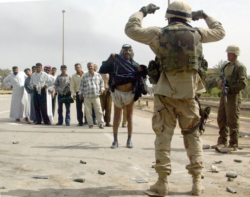 A US soldier orders an Iraqi man to lift his robe, fearing a suicide bomb attack, on Baghdad's al-Durra highway, in this file photo from April 10, 2003 