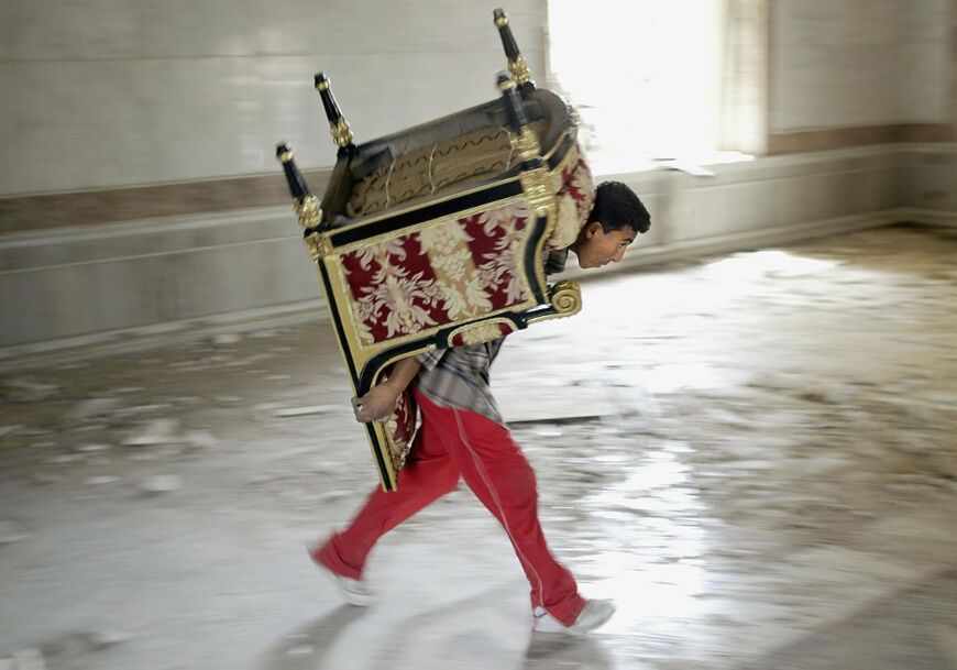 An Iraqi looter carries away a chair in Saddam Hussein's main palace in Baghdad, in this file photo from April 9, 2003 