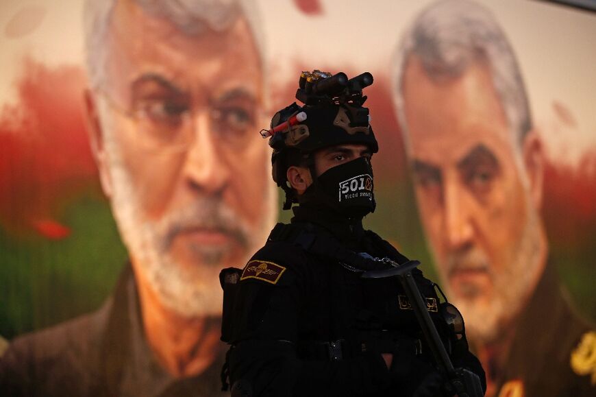 A member of Iraq's Hashed al-Shaabi stands guard in front of a banner depicting slain Iraqi commander Abu Mahdi al-Muhandis, left, and Iranian Revolutionary Guards commander Qasem Soleimani, near Baghdad's International Airport on January 2, 2023 