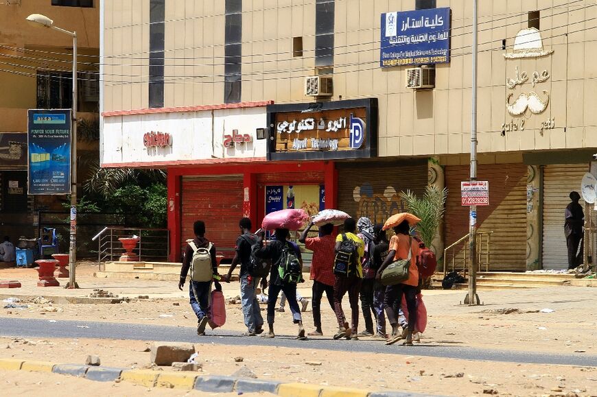 People carry their belongings in Khartoum on Sunday as fighting continues between rival forces