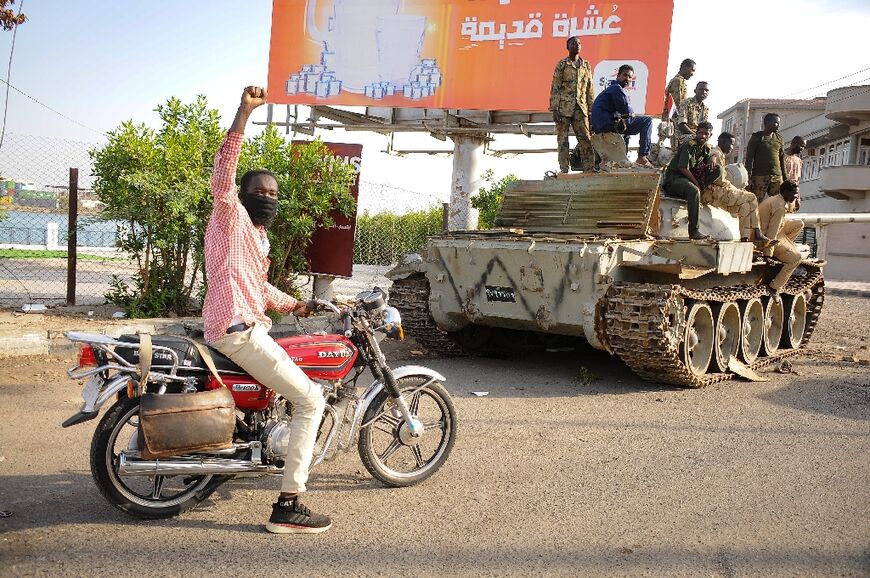 A man raises his arm in support as he drives near Sudanese army soldiers loyal to army chief Abdel Fattah al-Burhan in the Red Sea city of Port Sudan on April 20